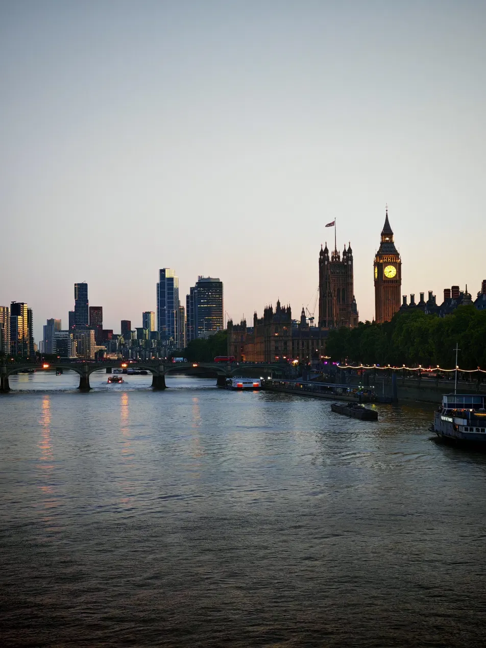 Westminster and the Elizabeth Tower at dusk from the Thames, with Westminster Bridge lit and river traffic moving downstream