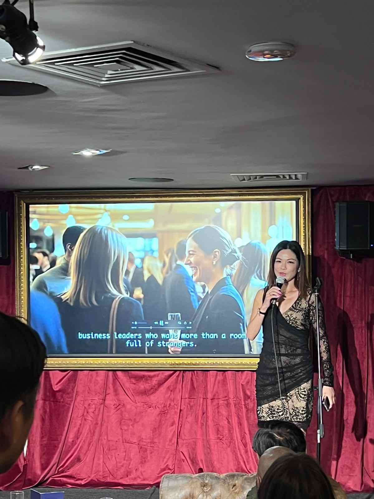 Gina Cheng hosting the V8 Nexus September Members' Evening, presenting to members beside the screen at the Grosvenor Rialto, Piccadilly